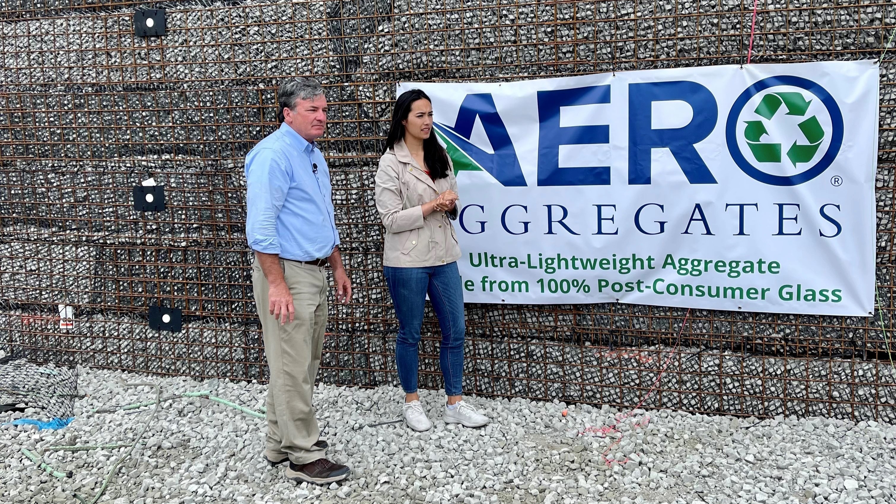 PennDOT Secretary Michael Carroll and NBC Today Show Reporter Emilie Ikeda stand in front of the temporary bridge structure that was built using recycled glass aggregate with an Aero Aggregates banner hanging on the structure behind them