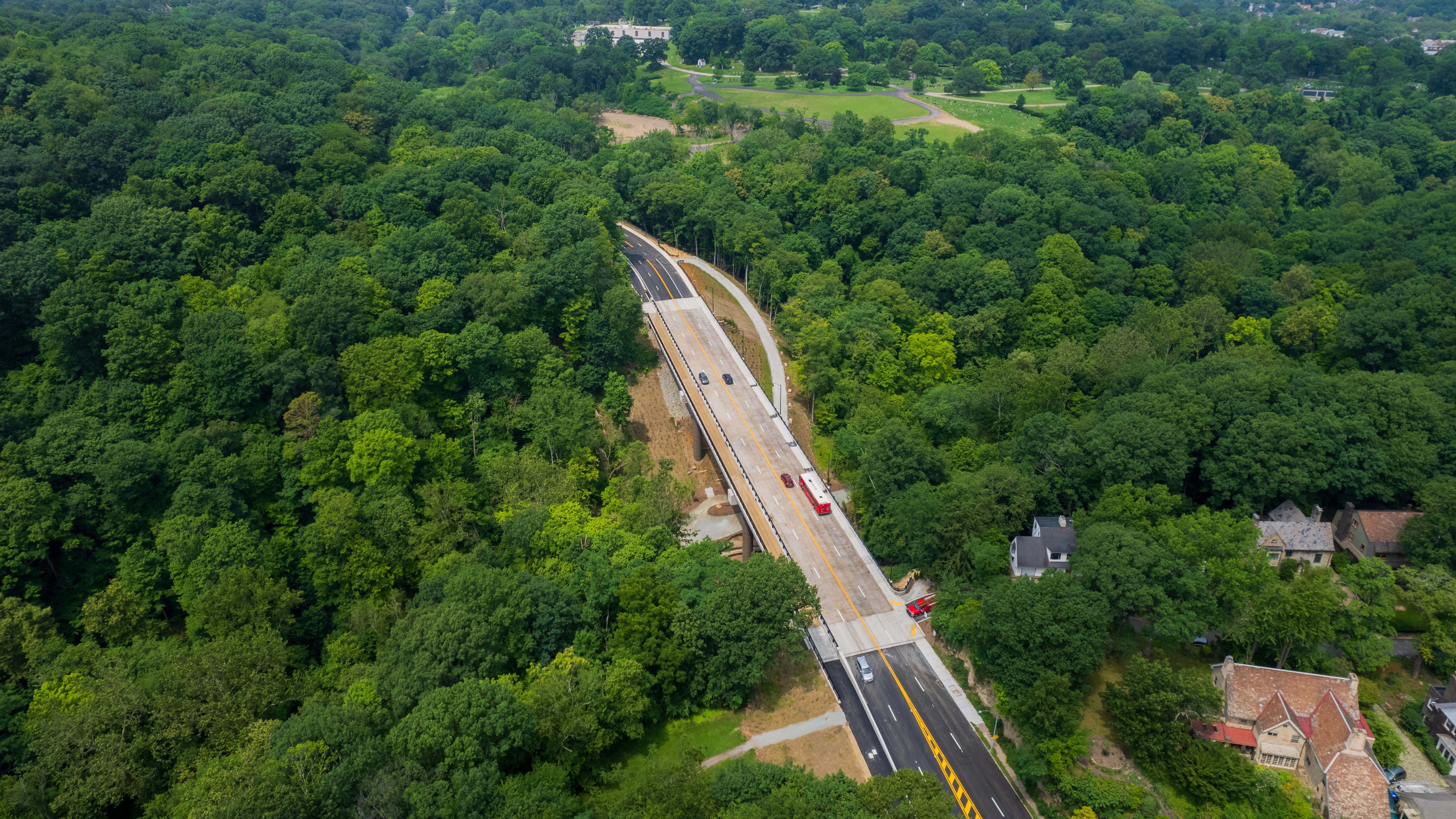 An aerial image of a red Pittsburgh Regional Transit bus and several other vehicles crossing the completed Fern Hollow Bridge
