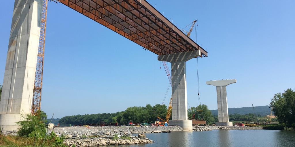 An image of a cranes being used to place beams on a bridge being constructed over a waterway