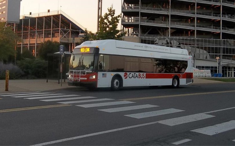 An image of a white and red mass transit bus parked outside a large sports stadium